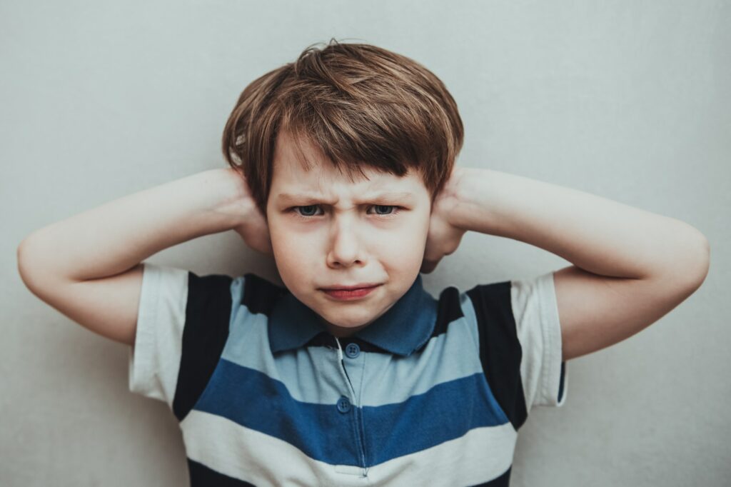 Child boy against gray background covering ears with hands. Domestic violence